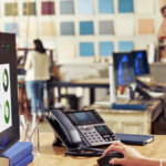 A professional woman working at a desk in a creative office environment with an HP Poly Edge V Series desk phone and data ...