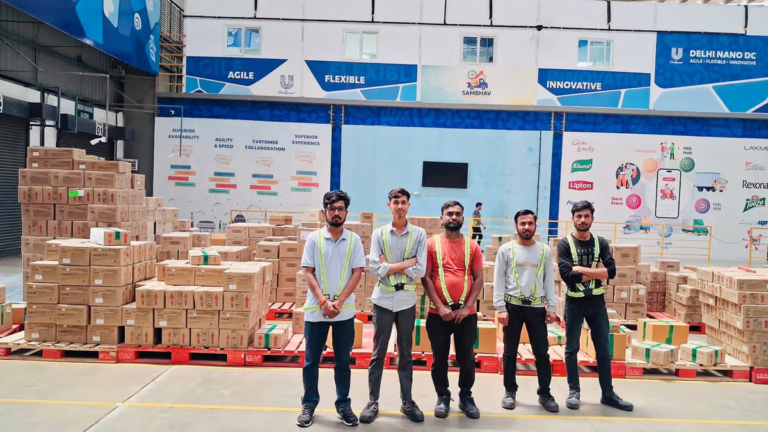 Five staff in safety vests standing by stacked boxes inside an HUL Delhi Nano DC facility in India.