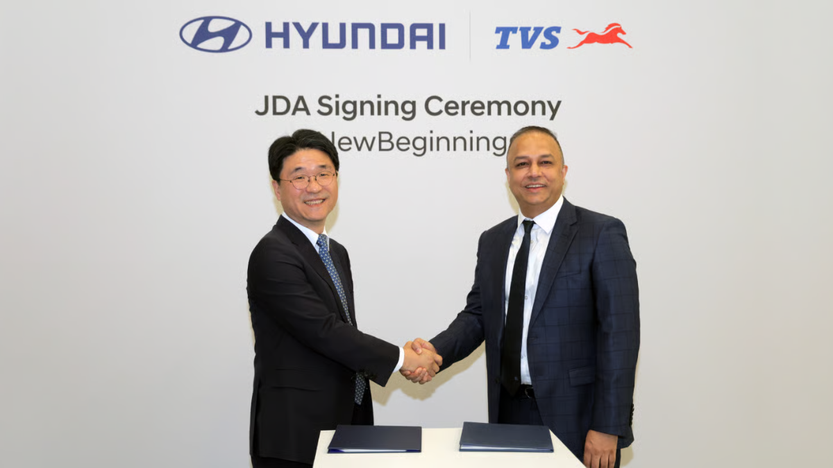 Hyundai's Joongsun Ko and TVS's Sharad Mishra shaking hands during a JDA signing ceremony for Indian electric vehicles.