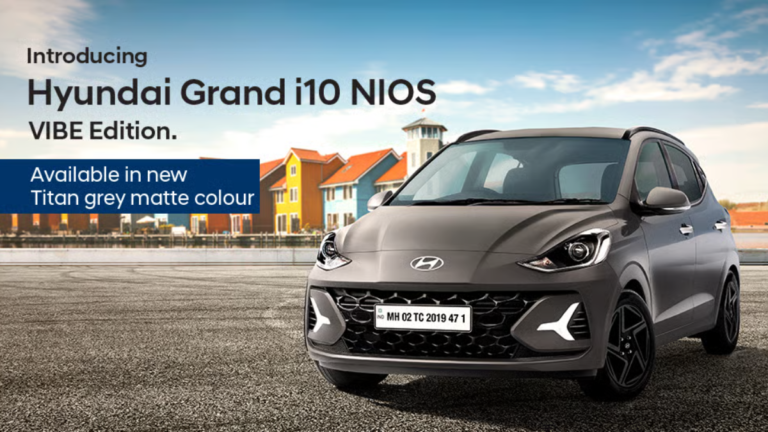 Front three-quarter view of the new Hyundai Grand i10 NIOS VIBE Edition in Titan Grey Matte parked against a coastal backd...