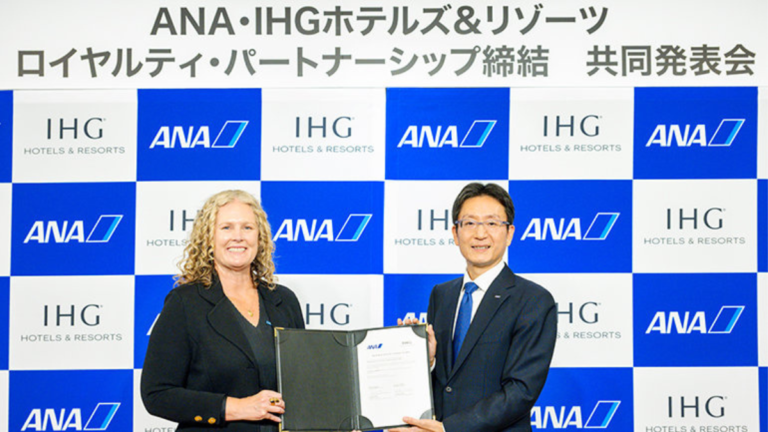 IHG and ANA executives holding a signed document against a branded backdrop for their India loyalty partnership.