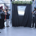 Executives in suits applaud while revealing a silver plaque for the 500th Kia India service workshop in Ahmedabad.