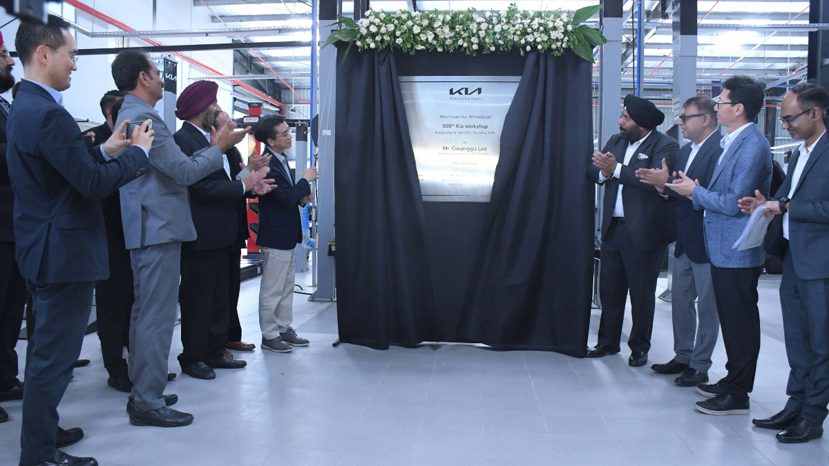 Executives in suits applaud while revealing a silver plaque for the 500th Kia India service workshop in Ahmedabad.