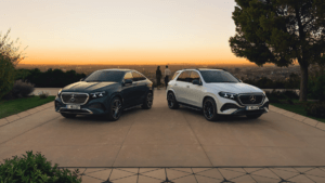 Front view of the 2026 Mercedes-Benz GLE SUV in Polar White and GLE Coupé in Emerald Green parked together during sunset.