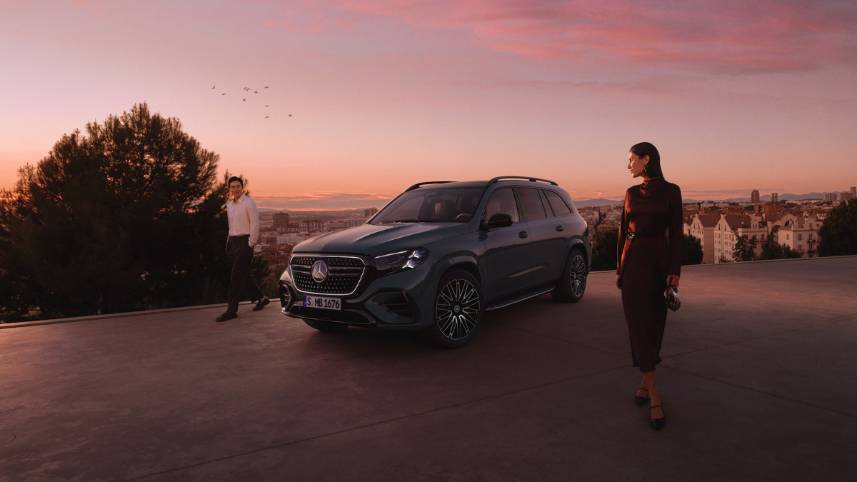 Front three-quarter view of the new Mercedes-Benz GLS flagship SUV in a dark emerald finish parked at a scenic lookout during sunset.