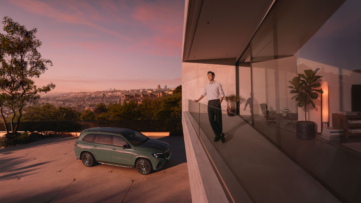 Profile view of the dark green Mercedes-Benz GLS parked at a modern minimalist villa overlooking a city skyline at dusk.