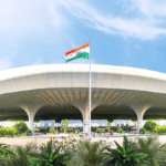 Daytime exterior view of Chhatrapati Shivaji Maharaj International Airport Terminal 2 in Mumbai with the Indian flag and lush landscaping.