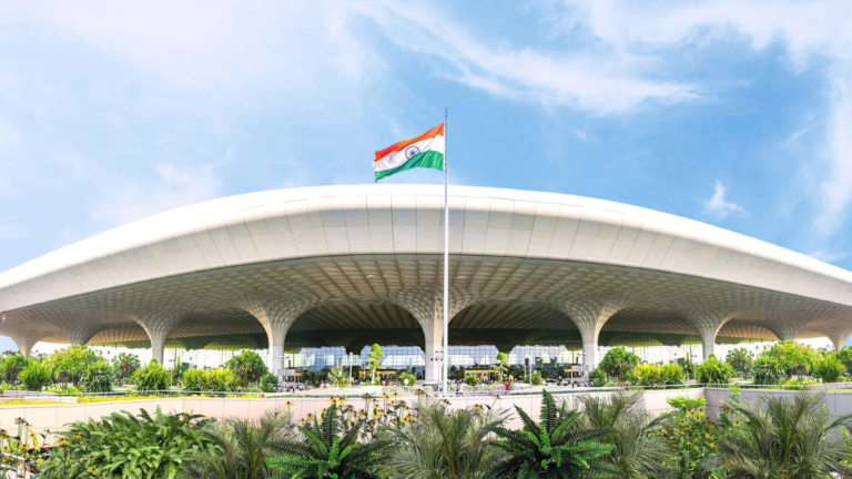 Daytime exterior view of Chhatrapati Shivaji Maharaj International Airport Terminal 2 in Mumbai with the Indian flag and lush landscaping.