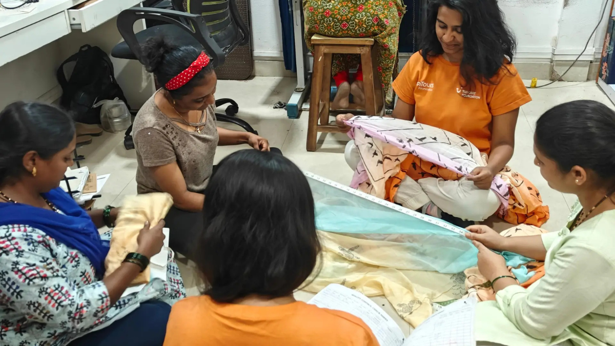 The ROI of Kindness: How TUI is Turning Local Guides into Global Entrepreneurs 2 Indian women artisans sitting on the floor in a workshop, measuring fabric and crafting handcrafted souvenirs as part of the PashooPakshee and TUI Care Foundation initiative.