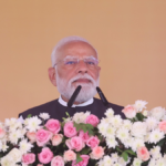 Prime Minister Narendra Modi speaking behind a podium covered in pink and white flowers during the Ganga Expressway launch.