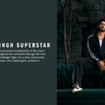 Ranveer Singh wearing a black tracksuit and Superstar sneakers while sitting on a green sofa in a jungle setting in India.