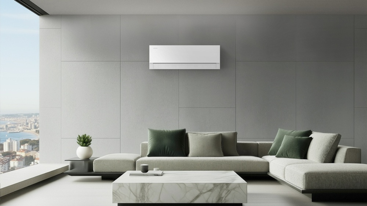 Minimalist white Samsung Bespoke AI WindFree Pro air conditioner wall-mounted above a grey L-shaped sofa in a modern luxury living room with a cityscape and bay view.