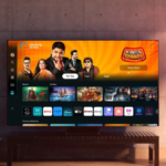 A detailed photograph of a large Samsung Smart TV in a contemporary living room, displaying the Samsung TV Plus user inter...