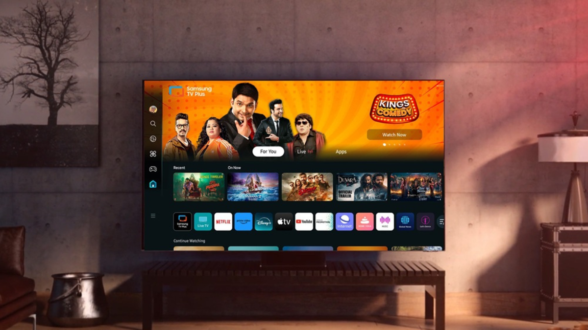 A detailed photograph of a large Samsung Smart TV in a contemporary living room, displaying the Samsung TV Plus user inter...