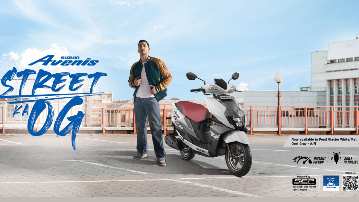A young man standing next to a white and grey Suzuki Avenis scooter on a sunny urban rooftop in India.