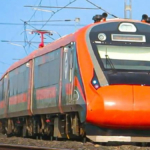 Orange and grey Vande Bharat Express train moving along a railway track in India with overhead power lines