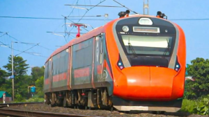 Orange and grey Vande Bharat Express train moving along a railway track in India with overhead power lines