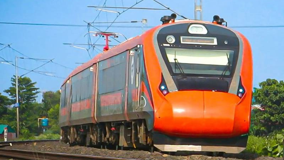 Orange and grey Vande Bharat Express train moving along a railway track in India with overhead power lines