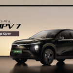 A sleek black VinFast VF MPV 7 electric vehicle with "Bookings Open" text, showcasing its modern V-shaped LED light bar and aerodynamic design.