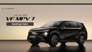 A sleek black VinFast VF MPV 7 electric vehicle with "Bookings Open" text, showcasing its modern V-shaped LED light bar an...