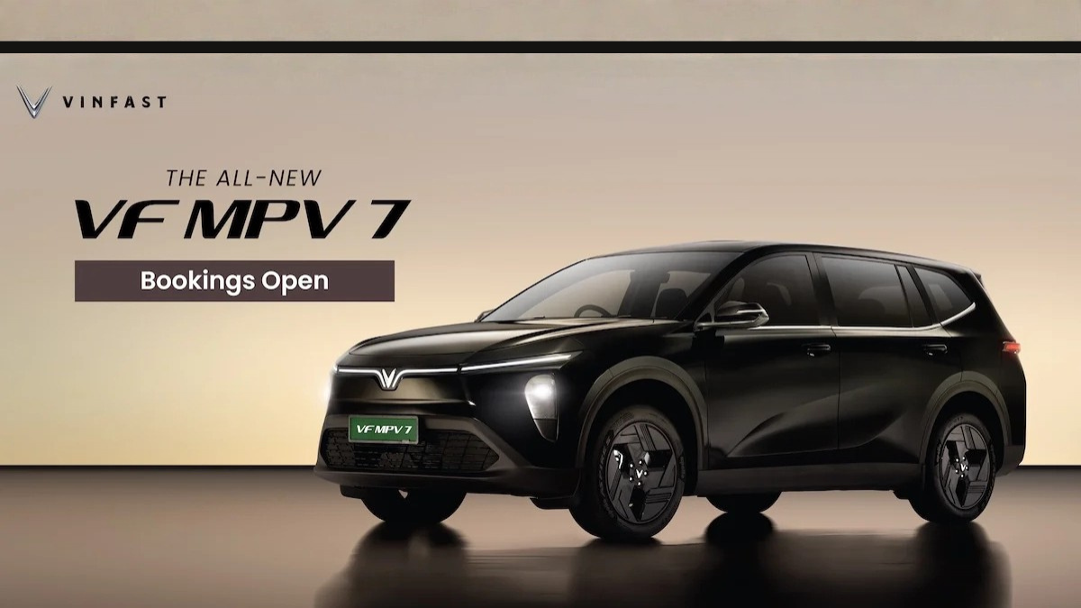 A sleek black VinFast VF MPV 7 electric vehicle with "Bookings Open" text, showcasing its modern V-shaped LED light bar and aerodynamic design.