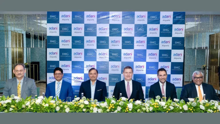 A 1,500-room deal brings Kimpton hotels to India 3 Six men in suits sit before an Adani Airports and IHG Hotels backdrop at a hospitality portfolio signing in India.