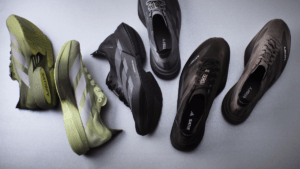 A top-down view of five adidas and Satisfy running shoes in olive green, earth brown, and black colourways.