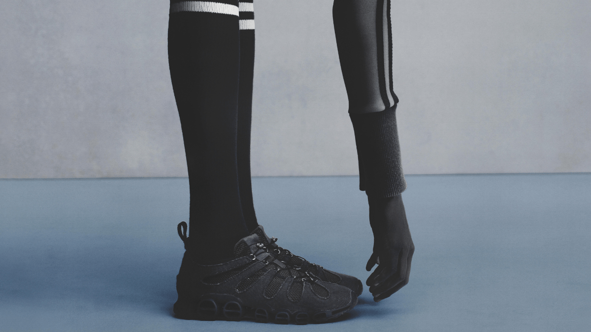 Is a raw anatomical sneaker the next big street style trend? 2 A close-up of a person wearing black knee-high socks and the stripped-back, all-black Avavav Megaride sneaker on a blue floor.