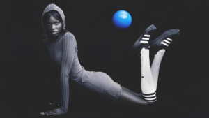 A model wearing a hooded dress, long white socks, and the black Modified Superstar shoes poses with a floating blue ball.
