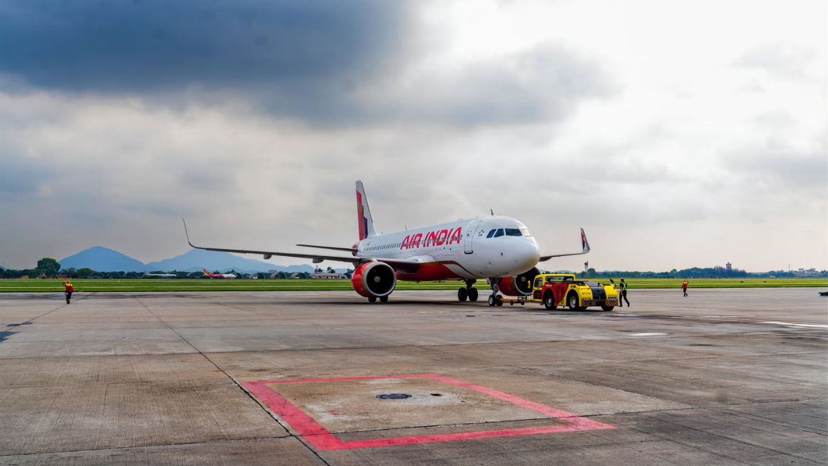 Air India A320neo plane being towed across the Noi Bai International Airport tarmac with mountains in the distance.