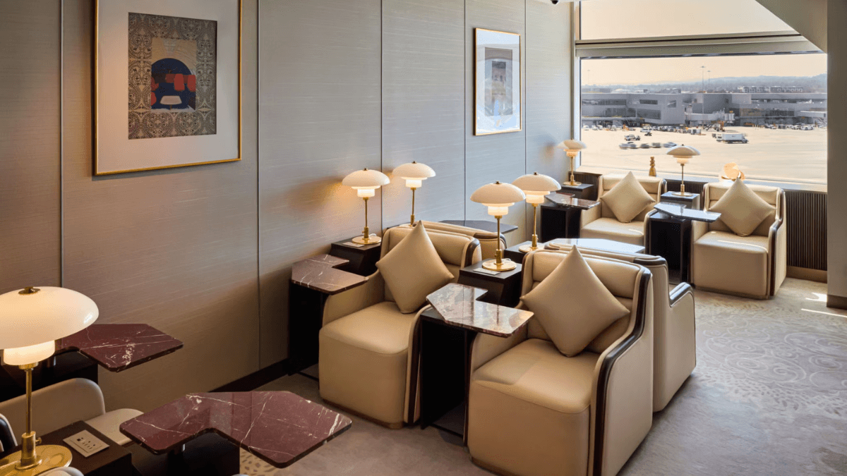 Plush ivory armchairs with marble side tables and individual lamps facing a large window overlooking the SFO airport tarmac.