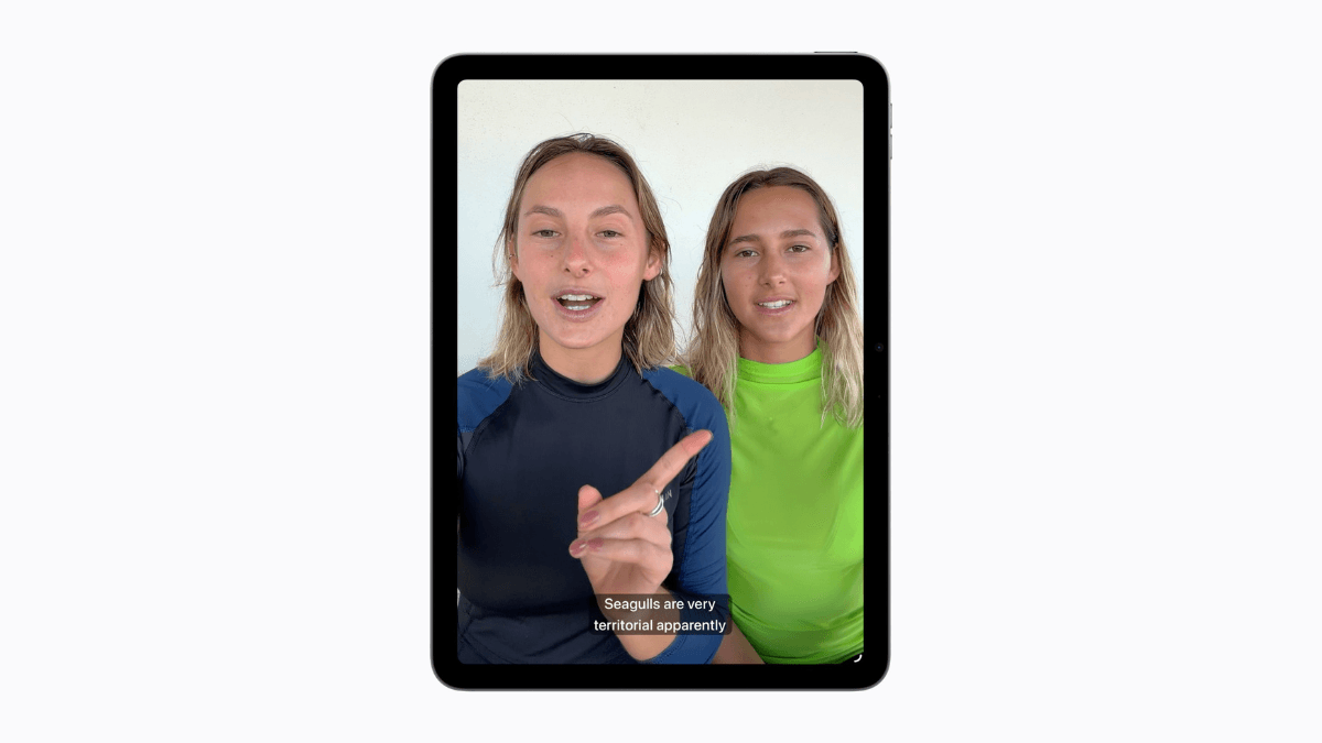 An iPad displaying two women speaking in a video clip with automated English subtitles running along the bottom border.
