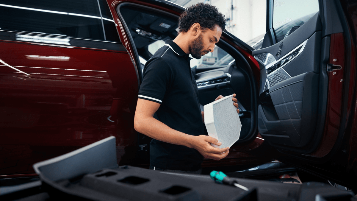 Is your luxury car ready for the intense Indian summer? 2 A technician holding a white cabin air filter next to the open front door of a red car during a BMW India maintenance check.