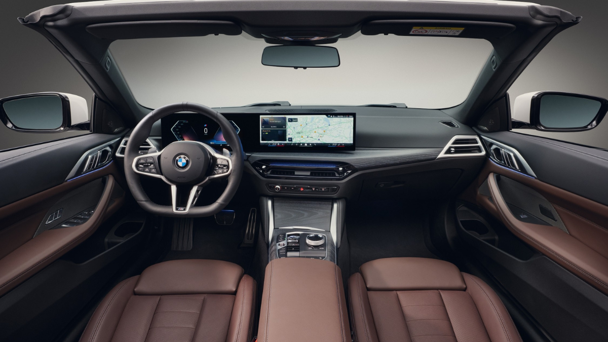 The modern cockpit of a BMW showing a large curved digital display, brown leather perforated seats, and an M steering wheel.