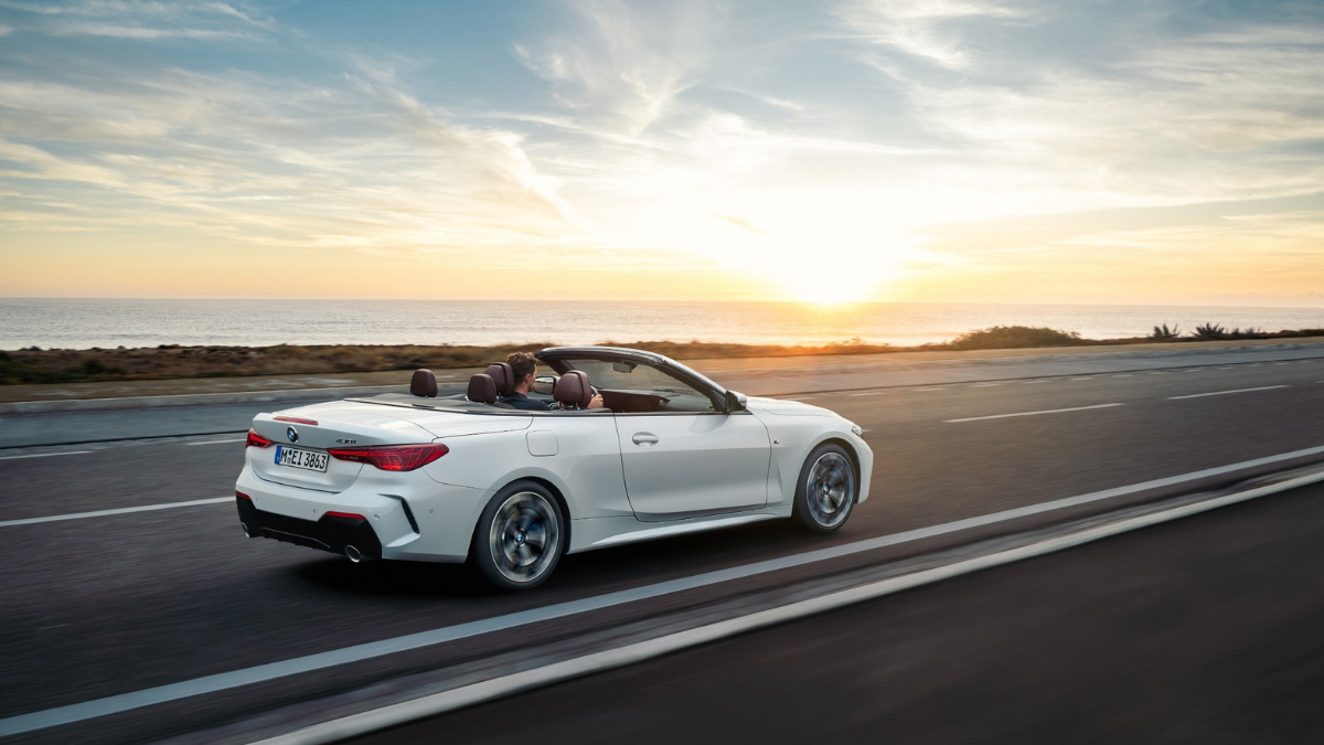 A white BMW convertible being driven along a coastal road at sunset, demonstrating M performance dynamics available in India.