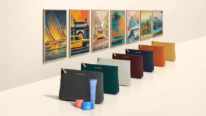Seven coloured amenity pouches in a row with gold zippers and Etihad logo, opposite seven matching framed travel art pieces.