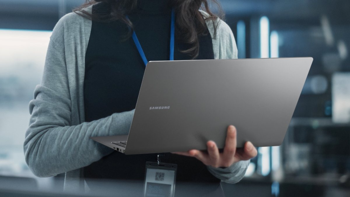 Galaxy Book6 Enterprise Edition Offers 24-Hour Battery 3 A professional holding a Mocha Gray Galaxy Book6 Enterprise Edition laptop in an office setting with a lanyard visible.