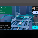 Car dashboard showing 3D buildings on a map next to a music player and message notification navigation.