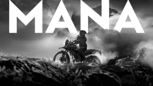 Rider in black kit on a Royal Enfield Himalayan motorcycle amidst misty Indian mountain peaks, with "MANA" text above.
