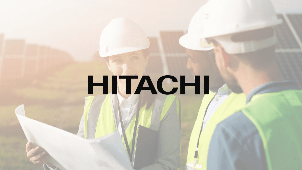 A ₹2,000 crore factory expands India's power grid 1 Engineers in safety gear review blueprints in a solar field with a large Hitachi logo overlaid, representing infrastructure.