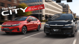 A red Honda City petrol sedan and a black eHEV hybrid sedan driving side-by-side on a city street in India.