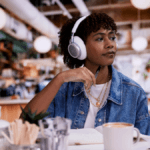 Woman wearing white JBL Live 780NC over-ear headphones in a cafe setting illustrating AI noise cancellation.
