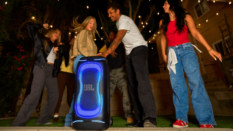 People dancing outdoors near a large JBL PartyBox 330 with blue neon lights during an evening party in India.