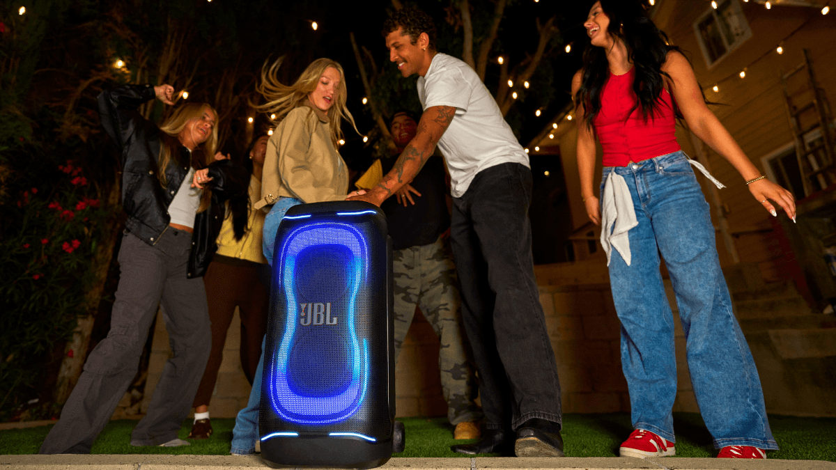 The pro-grade speaker built to last longer than your car 1 People dancing outdoors near a large JBL PartyBox 330 with blue neon lights during an evening party in India.