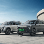 Silver and matte grey Kia Clavis EV SUVs parked side-by-side, the grey one connected to a wall charger in India.