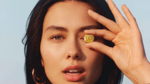 Woman holding a brass Lee button over her eye outdoors, reflecting the denim brand's new licensing era in India.