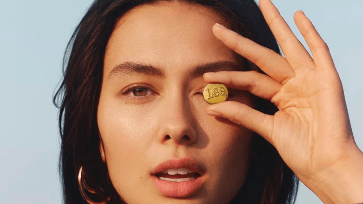 Will a new owner change how your next pair of jeans fits 1 Woman holding a brass Lee button over her eye outdoors, reflecting the denim brand's new licensing era in India.