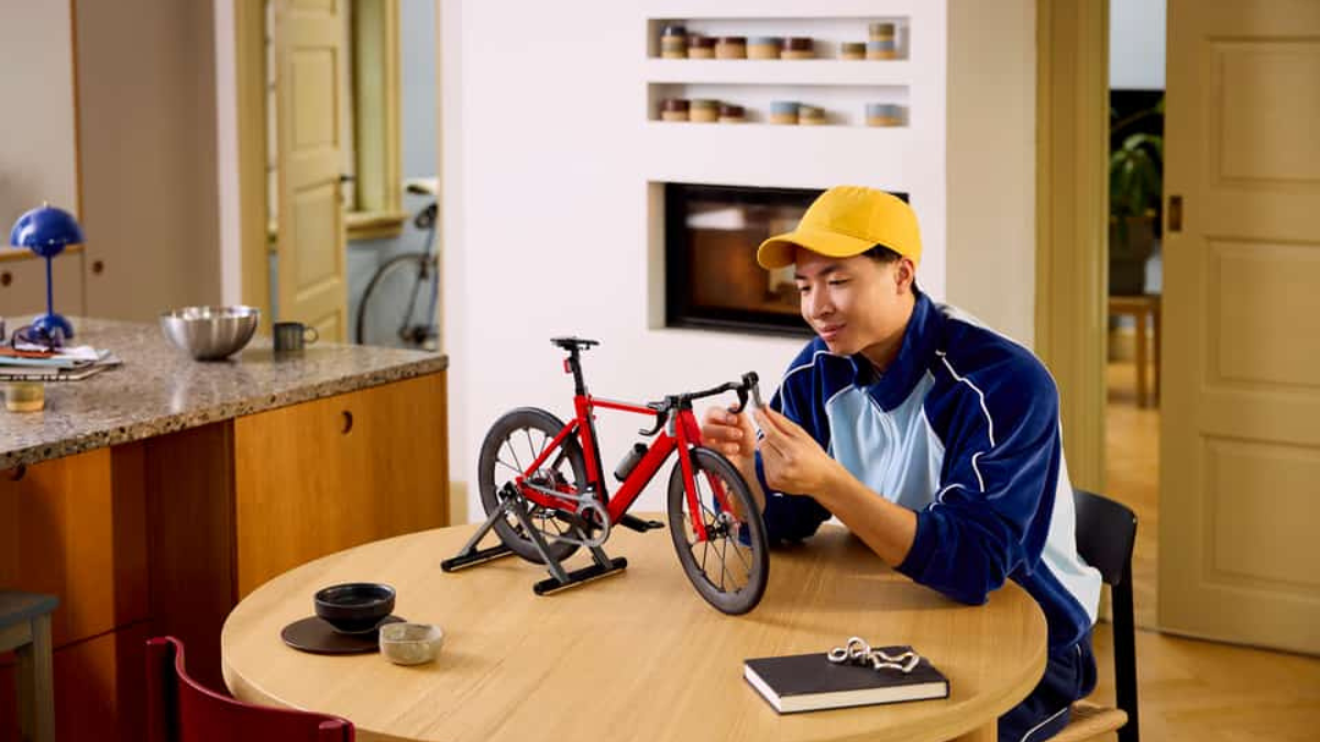 Adult builder adjusting handlebars of a red LEGO Icons Road Bike set on a dining table indoors