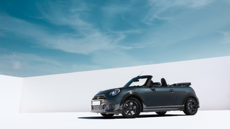 Dark grey MINI Convertible parked with the roof down against a white wall under a blue sky, showcasing the new India launch.