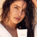 Priyanka Chopra Jonas in a white robe with wet hair holding an Anomaly tube for her India haircare brand growth.